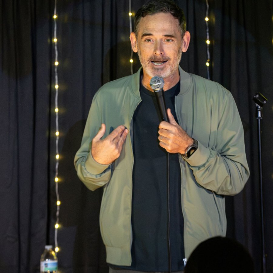 Andy Hendrickson mid-joke on stage under string lights